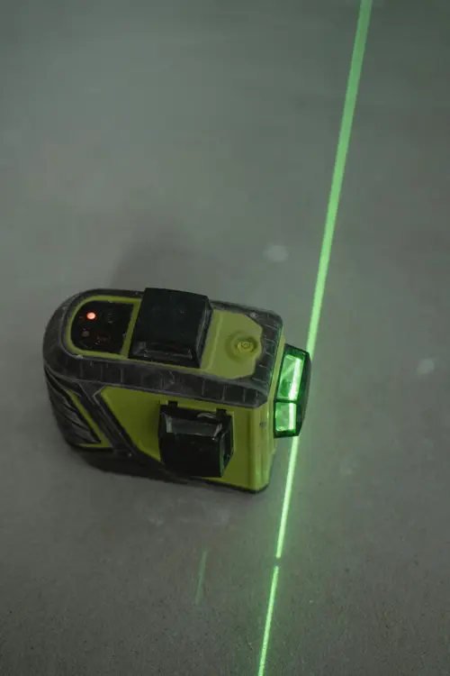 logo Grön laserpass på ett betonggolv som markerar en rak linje för mätning och byggarbete.