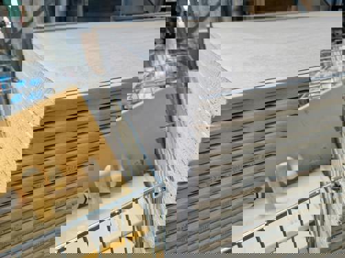 logo Närbild på en stapel ljusa gipsskivor i ett byggvaruhus. Skivorna är märkta med mått och ligger prydligt staplade, redo för försäljning. I förgrunden syns även några gula handverktyg i en metallkorg.