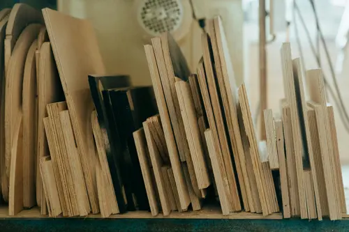 logo Bilden visar en samling faner- eller plywoodskivor i varierande dimensioner, prydligt uppställda på högkant i en verkstad. Skivorna används ofta inom snickeri och byggprojekt för möbler, inredning eller konstruktion.