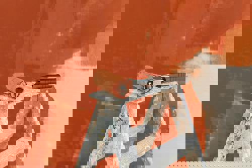 logo Målarroller på en stege/målarbock framför en vägg som målas i terrakottafärg.