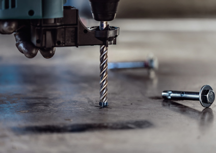 Borrmaskin borrar i betong med synliga skruvar på ytan.