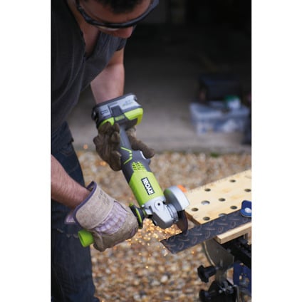 Person använder en grön batteridriven vinkelslip från Ryobi, gnistor flyger från metallplatta. Använder skyddsglasögon och handskar.