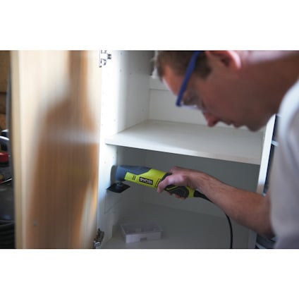 Person använder ett grönt elektriskt Multiverktyg från Ryobi i ett öppet skåp.