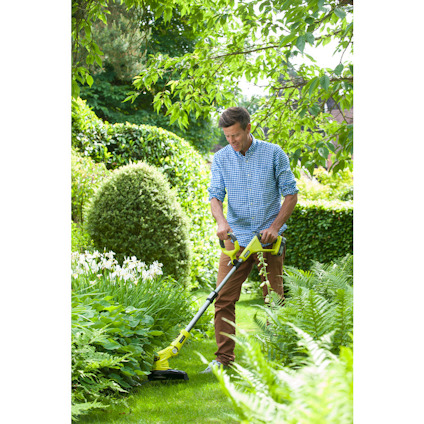 Man trimming garden plants with a yellow cordless grass trimmer, surrounded by greenery and bushes.