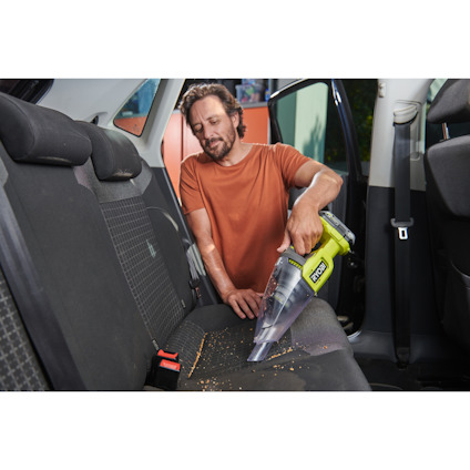En person i orange tröja använder en Ryobi handdammsugare för att rengöra baksätet i en bil.