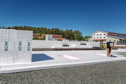 Stora vita polystyrenblock staplade på en grusplan; en person böjer sig ner på blocken.