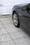 Svart bil parkerad på ljusgrå stenlagd uppfart framför vit garageport.