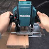 En person använder en Makita-handöverfräs för att bearbeta en träbit.