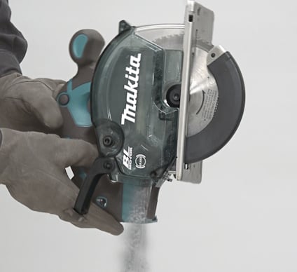 Person i handskar håller en Makita cirkelsåg i färd med att kapa material.