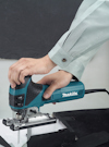 En person använder en blå Makita sticksåg för att såga i en vit yta.