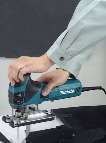 En person använder en blå Makita sticksåg för att såga i en vit yta.