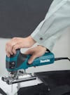 En person i skjorta använder en elektrisk sticksåg av märket Makita för att såga i vit materialbit.