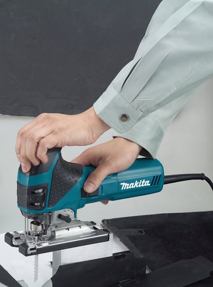 En person i skjorta använder en elektrisk sticksåg av märket Makita för att såga i vit materialbit.