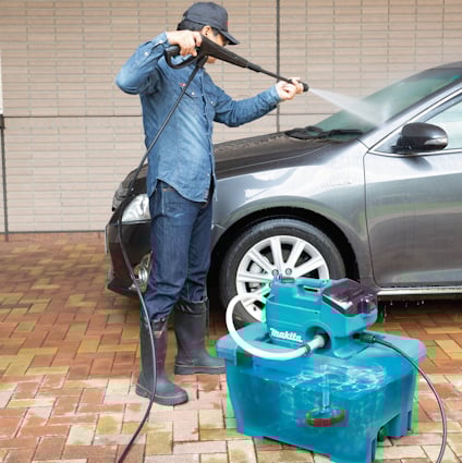 Person tvättar en bil med en högtryckstvätt bredvid en blå Makita-maskin.