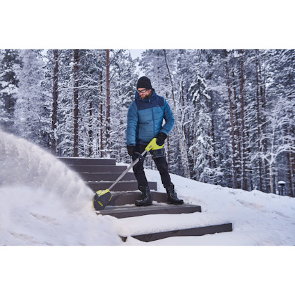 Person i vinterkläder använder en snöslunga av märket RYOBI på snötäckta trappsteg i skogsmiljö.