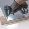 En person använder en blå och svart borrmaskin för att borra i en metallplatta ovanpå en träyta.