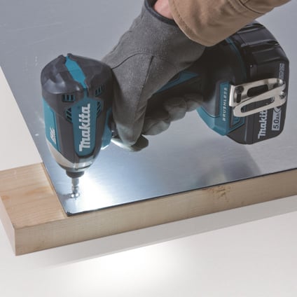 En person använder en blå och svart borrmaskin för att borra i en metallplatta ovanpå en träyta.