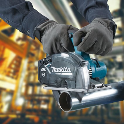 Händer i handskar håller en Makita cirkelsåg som skär genom ett metallrör.