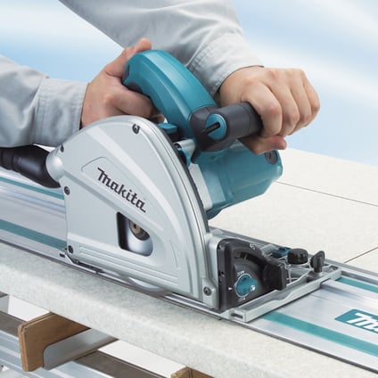 En person använder en Makita cirkelsåg som glider på en skena över en platta yta.
