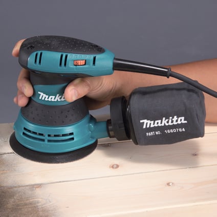 Person använder en blå och svart Makita slipmaskin på träyta.