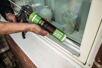 En person tätar springan mellan fönster och karm med fogmassa och fogpistol.