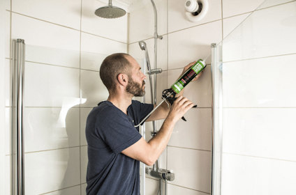En person applicerar fogmassa med fogpistol i en duschkabin.