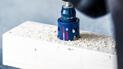 Borr som borrar genom träbit med spån runt hålet.