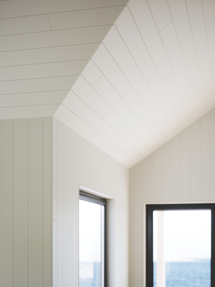 Vitt träpaneltak och väggar i ett rum med fönster som visar utsikt över vatten.