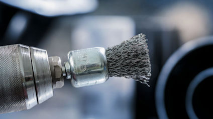 Stålborste fäst på borrmaskin, suddig bakgrund.