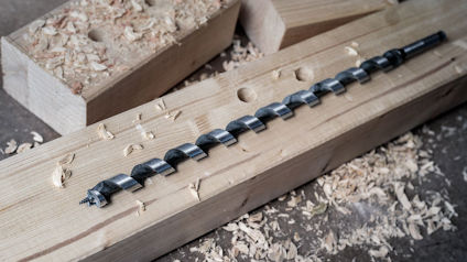 Borrbits i spiralform på ett trästycke med träspån runt omkring.