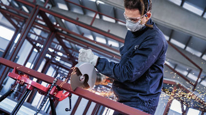 Person skär metall med kapsåg i industriell miljö, gnistor flyger.