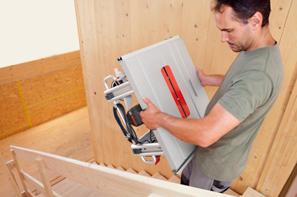 Person bär en bordscirkelsåg uppför en trätrappa.