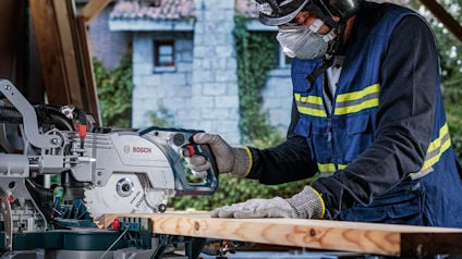 Person som använder en Bosch-märkt såg för att skära en träplanka. Använder skyddsutrustning.