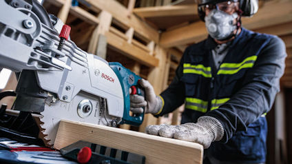 Person i skyddsutrustning använder ett Bosch elverktyg för att såga trä.