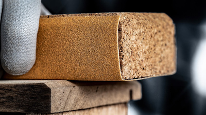 Hand i handske håller ett slipblock mot en träbit.