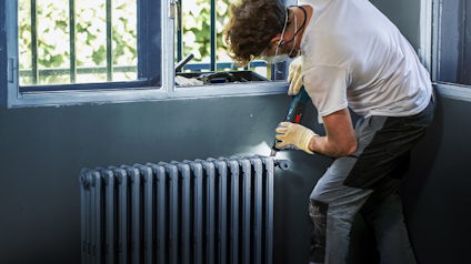 Person som arbetar vid ett element nära ett fönster, bär verktygsbälte och skyddsutrustning.