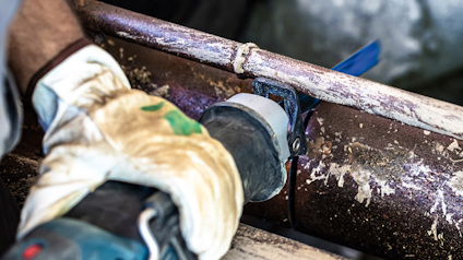 En hand med handske håller en blå och svart kapmaskin mot ett rör för att göra ett kap.