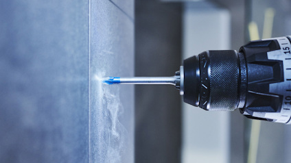 Borrmaskin borrar i en grå vägg med en blå borr.