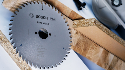 Cirkelsågsklinga från Bosch för proffs användning inom träbearbetning, omgiven av träplankor och träskivor.