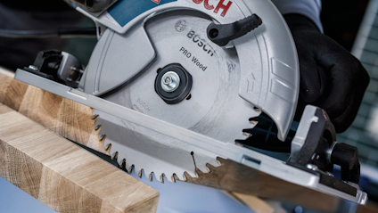 Cirkelsåg med märkningen "Pro Wood", skär genom en träbräda. Säkerhetshandskar syns på användarens händer.