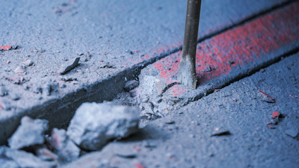Jackhammer bryter upp betong med sprickor och röd linje i marken.
