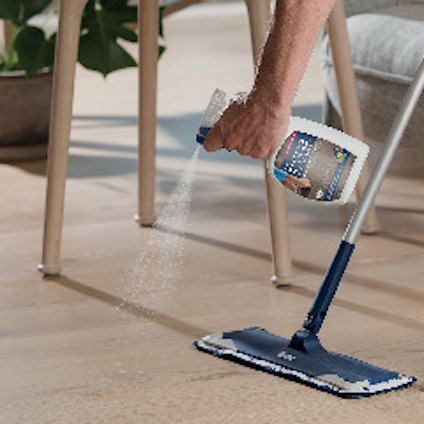 En person använder en Bona-golvborste och sprayflaska för att rengöra ett ljust trägolv.
