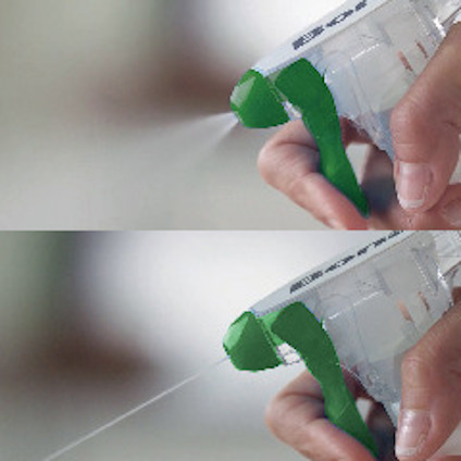 En hand trycker på en sprayflaska med genomskinlig vätska och grön plastdetalj, vätskan sprutar ut.
